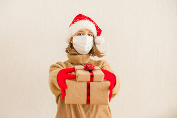 girl in a santa hat and a medical protective mask holds gifts in her hands. New Year 2021