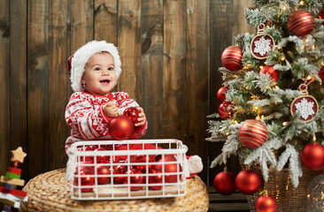 Smiling baby girl with christmas balls next to christmas tree