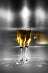 Two glasses with golden champagne on a sparkling metal background.