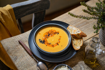 Vegetarian autumn pumpkin cream soup with black seeds, toasted bread on wooden rustic table. Organic, country food style. Vegan healthy dish. Copy space.