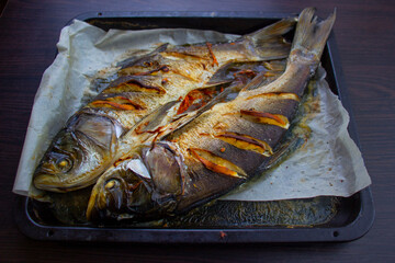 Baked fish with lemons on a baking sheet. Silver carp.