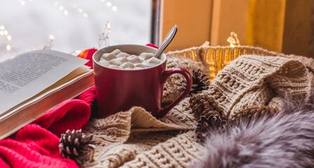 Red Cup with cocoa and marshmallows on a wooden table with scarves old book home comfort
