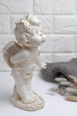 White plaster figurine of an angel against a brick wall with a knitted gray scarf and dried flowers hare tails.