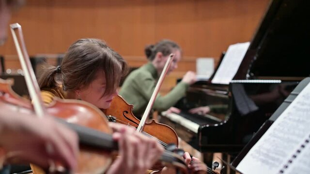 Focus on a young woman playing the violin with a string quartet and grand piano. Selective focus
