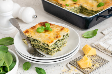 A piece of lasagna with spinach, ricotta and bechamel sauce on a white plate. Traditional italian dish. Selective focus.