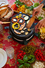 Raclette table setting with raclette machine and food ingredients. Swiss raclette served with different cheeses, fish, sald, mushrooms, paprika, bread. Self-service party.