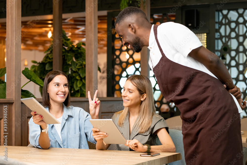 Poster young smiling waiter in uniform bending over table and looking at happy girl