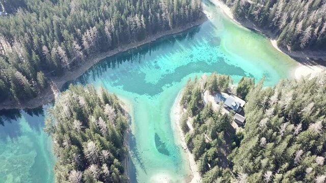 A drone shot of anAlpine valley in Austria. The valley has a Green Lake in the middle.  A headland in the middle of the lake. The algae give the lake distinctive color. Early spring in the mountains
