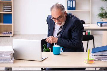 Obraz premium Old male employee drinking alcohol in the office