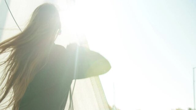 A young athlete learns to set sail on a yacht during a training race on sailing vessels. Bright glare of the sun in the camera.