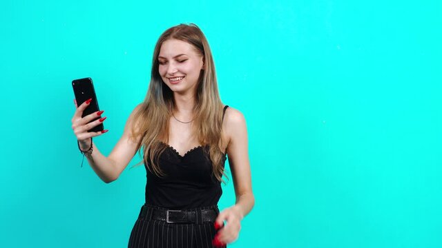 The puzzled teenager but with a smile on her face speaks pretentiously on the phone. Happy with the news received. Charming girl, dressed in black T-shirt with cleavage, in the studio on a blue