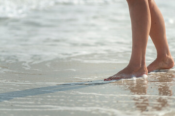 Feminine barefoot legs on wet sand next to sea water