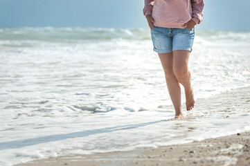 Barefoot middle age woman in summer casual outfit wolking on sea coast line