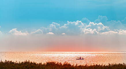 Coastline with one kajak silhuette on red water colored with setting sun under stunning neon blue cloudy sky