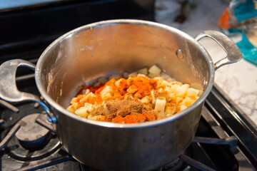 A stainless steel pot on a stove in a restaurant kitchen with the mixture ingredients for samosa. The dish contains small chopped pieces of potatoes, onions, carrots and Indian spices.  