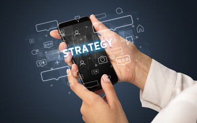 Female hand typing on smartphone with STRATEGY inscription, social media concept