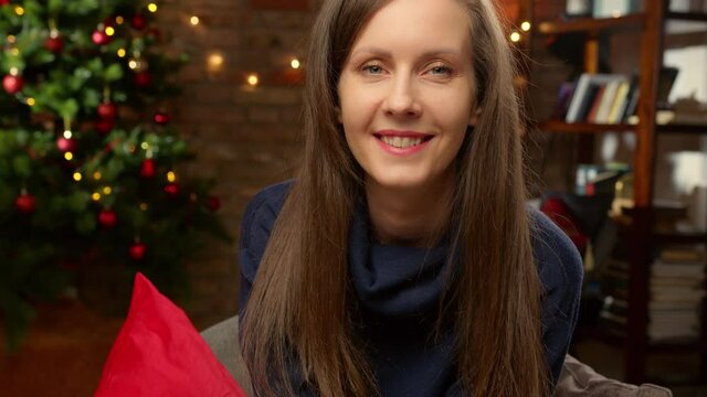 Winter portrait of young woman at home smiling, Christmas tree in background.