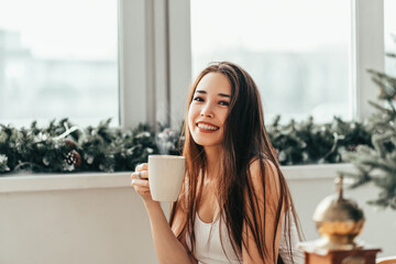 Beautiful smiling girl early in the morning drinking fragrant hot coffee cappuccino