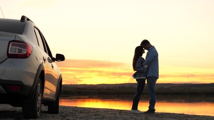 happy lovers travelers man and woman stand next to car and admire beautiful sunset on beach....