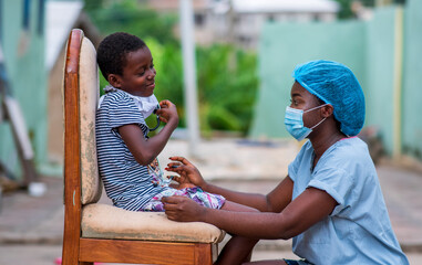 Cheerful African nurse in protective face mask seeing a child outdoor-concept on child health care in covid-19 pandemic