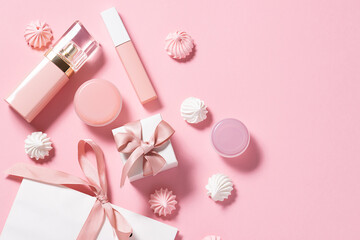 Obraz na płótnie Canvas Gift set of cosmetic with paper bag ,sweet meringue cookies and and ribbons on pink pastel background. St. Valentines Day concept. Festive cosmetic sale concept.