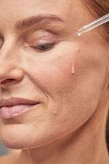 Smiling lady applying essential oil on facial skin and looking down