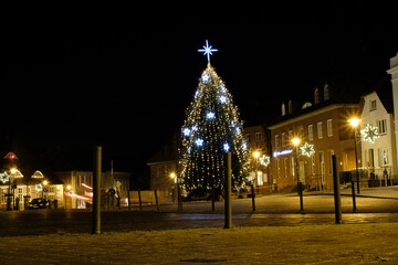 Fototapeta na wymiar on a market place of a small town stands an illuminated Christmas tree