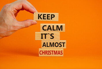 Christmas time. Male hand placing wooden blocks with words 'keep calm it is almost christmas'. Beautiful orange background. Copy space. Business and christmas concept.