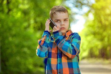 An emotional child is talking on a mobile phone in a Park on a Sunny summer day.