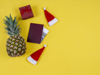 
Pineapple, passport and gift.

Pineapple, passport, ticket, two Santa hats and a gift lie on the left on a yellow background with a place for text on the right, top view.