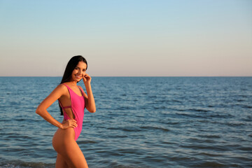 Fototapeta na wymiar Beautiful young woman in pink stylish swimsuit on beach. Space for text