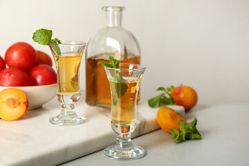 Delicious plum liquor with mint and ripe fruits on light table. Homemade strong alcoholic beverage