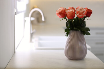 Vase with beautiful roses on countertop in kitchen, space for text. Interior design