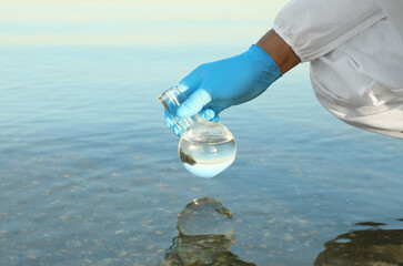 Scientist with florence flask taking sample from river for analysis, closeup