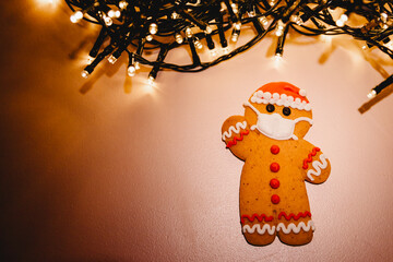 Special New Year's background with elements of the Christmas cookies, festive lights, Christmas ornaments: gingerbread in the shape of Santa Claus with a protective medical