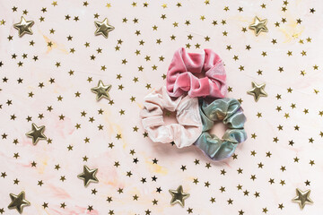 Three trendy velvet pink and holographic shiny metallic scrunchies and golden stars confetti on pink background. Diy accessories and hairstyles for Christmas and New Year party concept, copy space