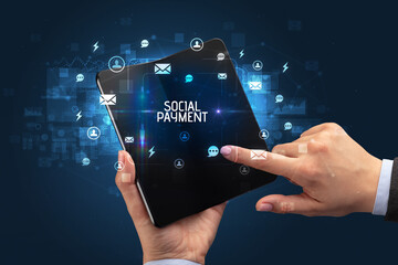 Businessman holding a foldable smartphone with SOCIAL PAYMENT inscription, social networking concept