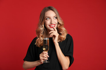 Happy young woman with glass of champagne on red background. Christmas celebration