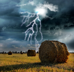 Picturesque lightning storm over field with rolled hay bales