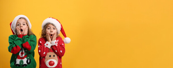 Kids in Christmas sweaters and Santa hats on yellow background, space for text