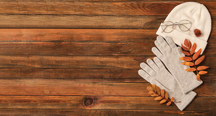 Flat lay composition with stylish woolen gloves and dry leaves on wooden table. Space for text
