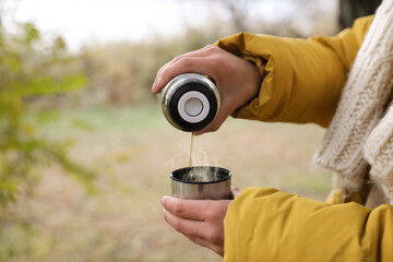 Woman pouring drink from thermos into cap outdoors, closeup. Space for text