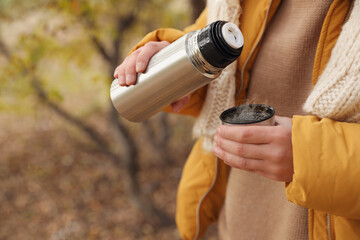 Naklejka premium Woman pouring drink from thermos into cap outdoors, closeup