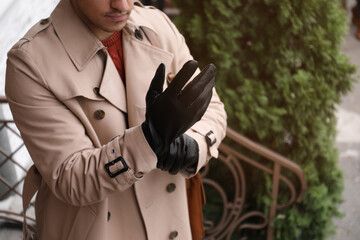 Stylish man putting on black leather gloves outdoors, closeup. Space for text