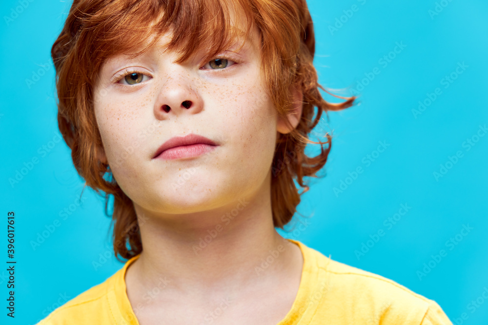 Wall mural Boy with red hair face close up yellow t-shirt childhood blue 