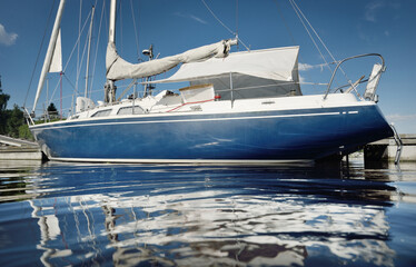 Classic blue sloop rigged yacht moored in marina with a sun cover. Cruising life, vacation, sailboat travel, sailing, recreation, leisure activity, sport, transportation, water surface texture © Alex Stemmer