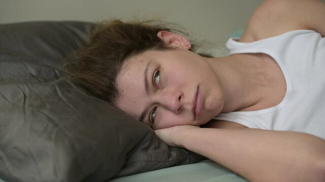 close-up of a young woman who is awakened by annoying noise from neighbors or the street and covers her head with a pillow