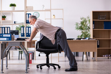 Old male employee doing physical exercises at workplace