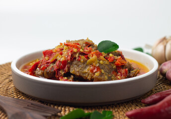 Dendeng Balado, Indonesian traditional beef cuisine from Padang, West Sumatra with slices beef cooked with some spices and a lot of chilies. served on ceramic plate and isolated white background.   