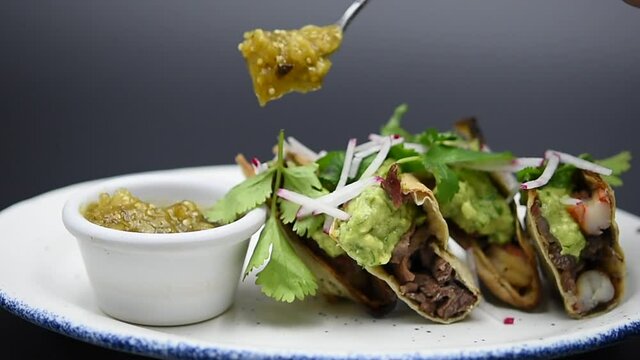 Colocando salsa verde a tacos mexicanos